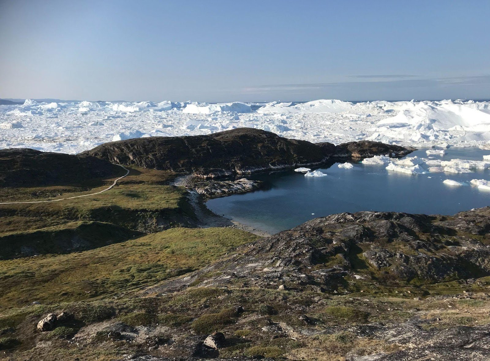 Fig. 1 This green plain within the Ilulissat UNESCO property holds 4,000 years of Inuit history. Now, erosion is accelerating as the permafrost beneath it melts (Source: Bo Albrechtsen, 2025).